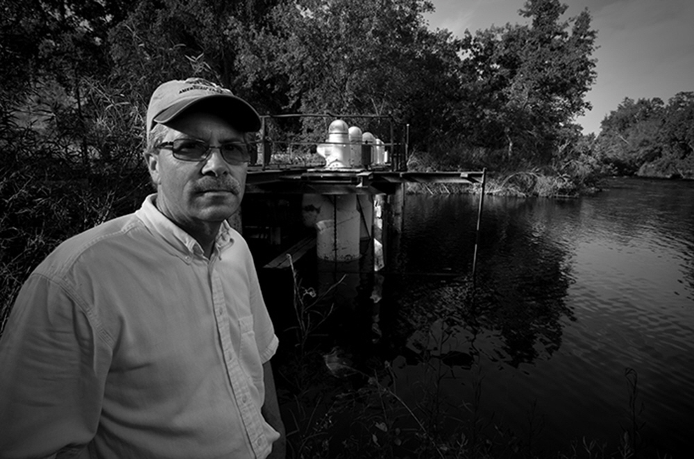 Illustrating the Kings mechanization, Professor Kent Kinney stands near huge siphon pumps that once transferred water beneath the river.